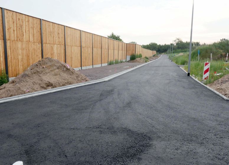 Foto: c/o Gemeindewerke Budenheim/Oliver Strott
Neuer Teil der Bertolt-Brecht-Straße im Neubaugebiet Wäldchenloch. Links Lärmschutzwand mit Flächen für private Stellplätze.